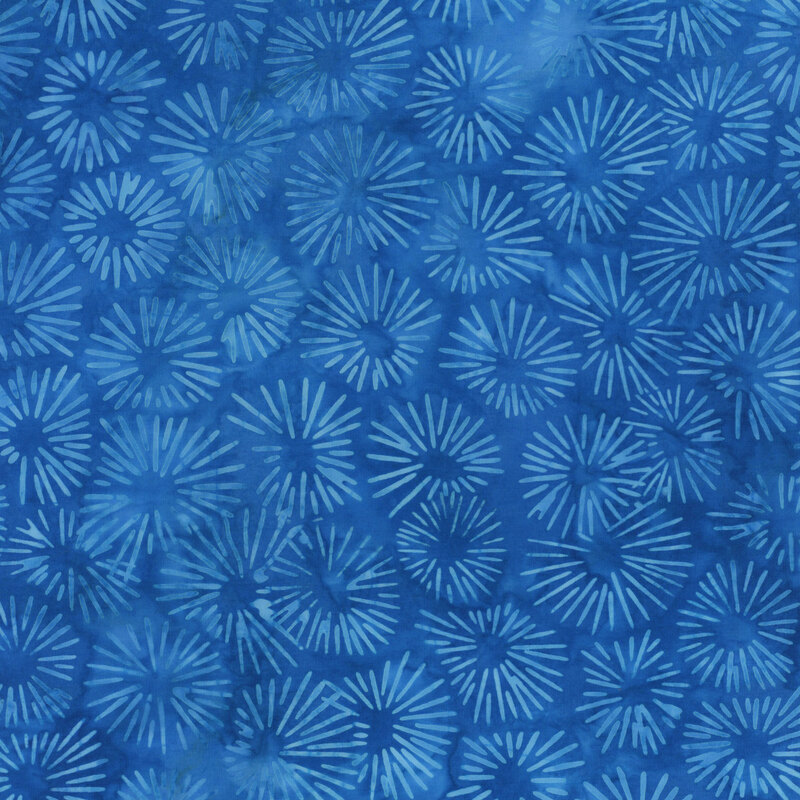 A blue mottled batik fabric with light blue sun bursts