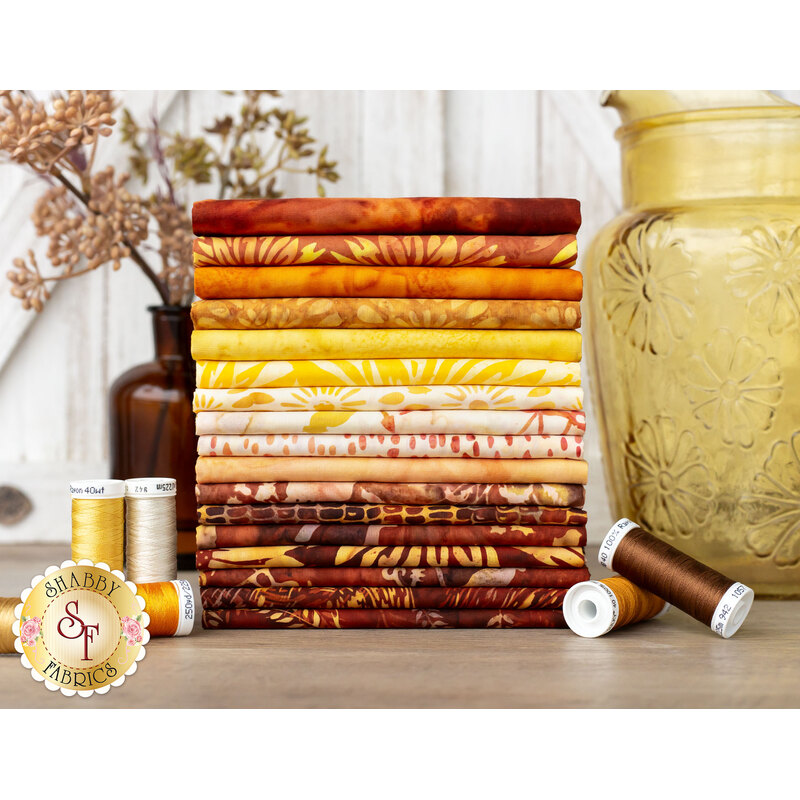 stack of fabrics in warm shades of yellow, orange, red, and brown on a wood table 
