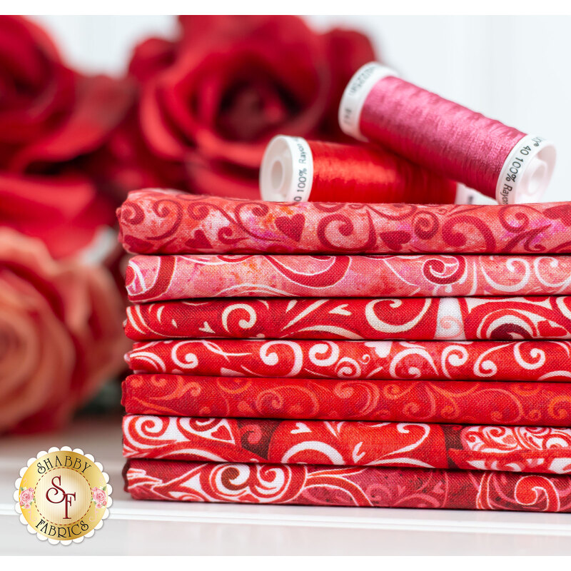 Swirls and hearts on red fabric stacked on a table with roses