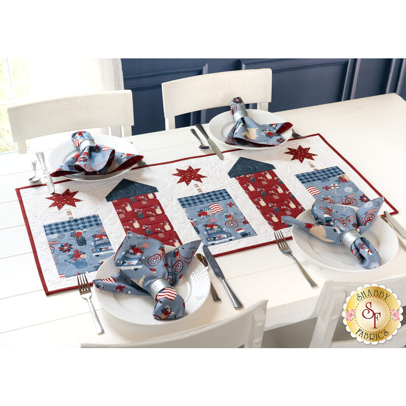 A white table with a festive table runner and four place settings with matching napkins on white plates