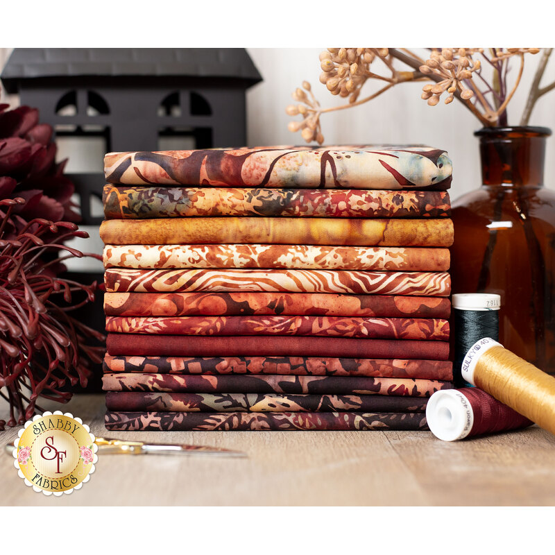 autumn themed batik fabrics surrounded by dried flowers and a tin black house