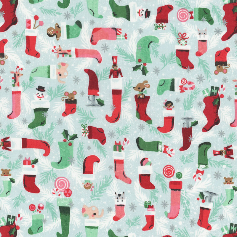 This fabric features red and green tonal Christmas stockings with toys and boughs on a light blue background with metallic silver accents.