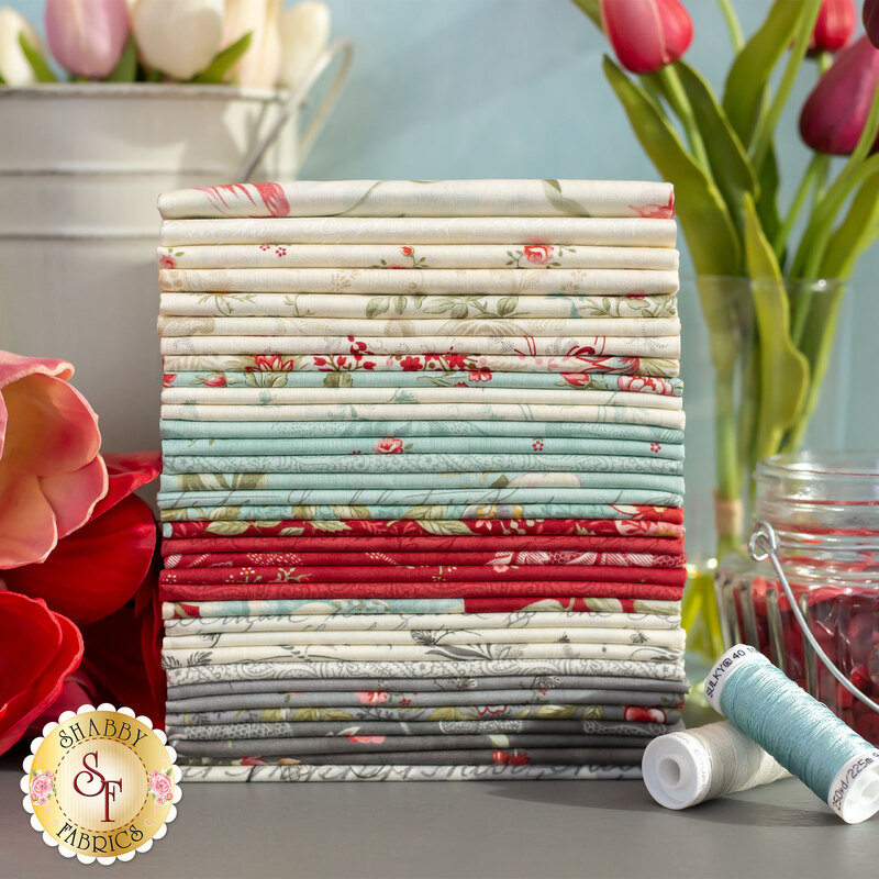 stack of fabrics in the Collections for a Cause - Etchings collection in shades of cream, blue, gray, and red, surrounded by tulips, thread and buttons