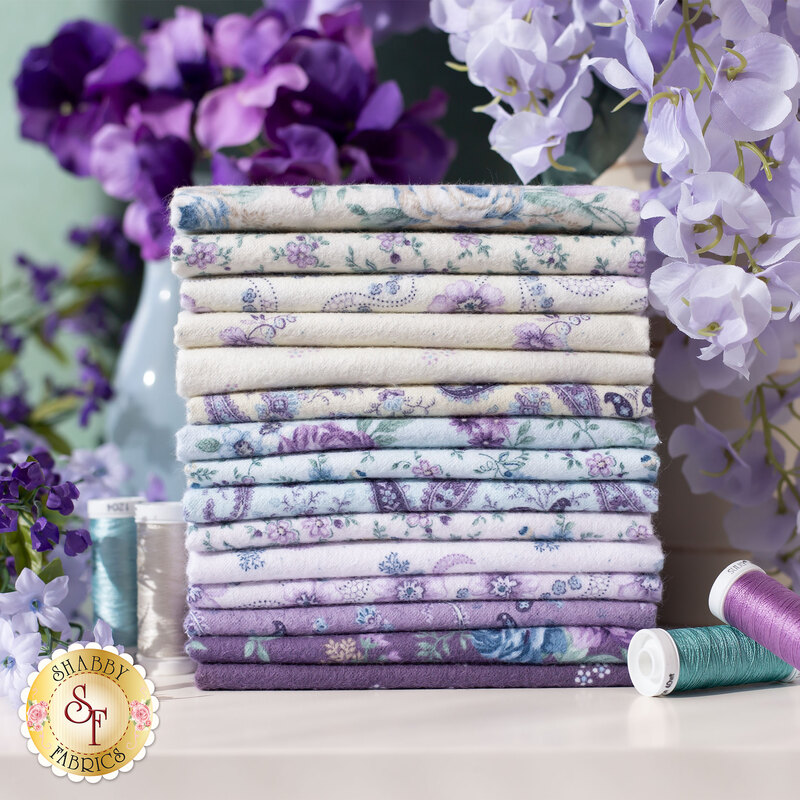 cream, pastel blue, lavender, and eggplant floral flannels stacked on a table with flowers