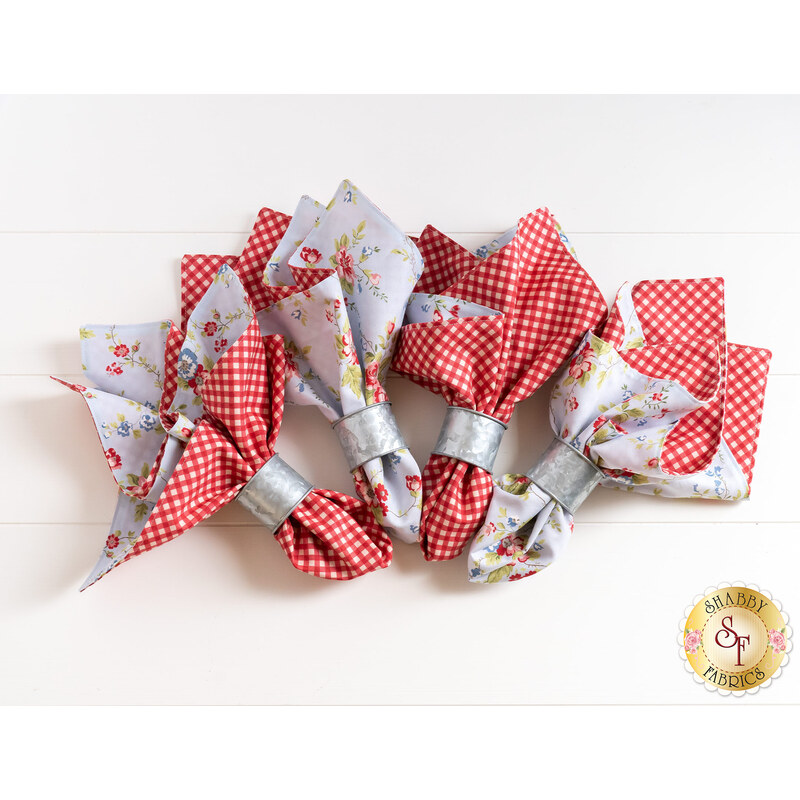 Reversible cloth napkins with red gingham fabric on one side and blue floral fabric on the other, in silver napkin rings.