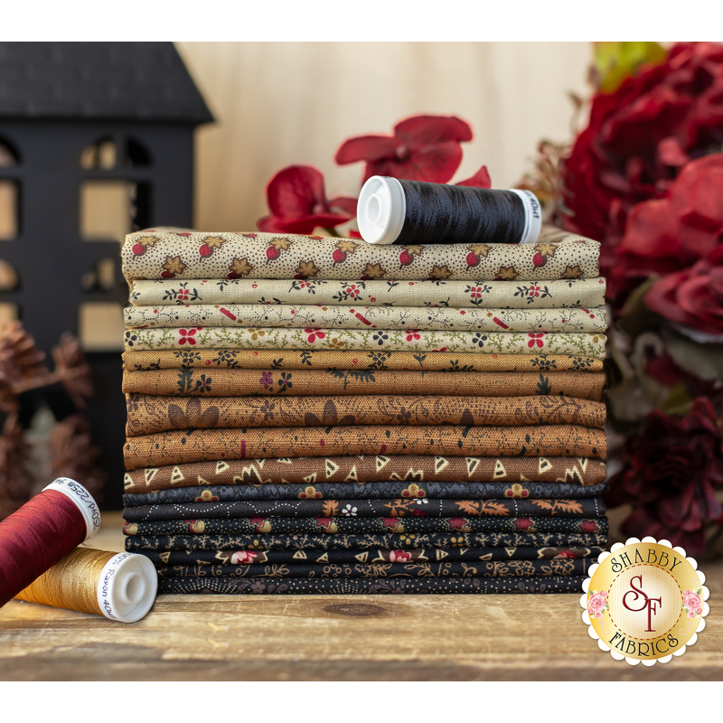 cream, tan, and dark brown and black fabrics with red floral accents stacked on a wood table.