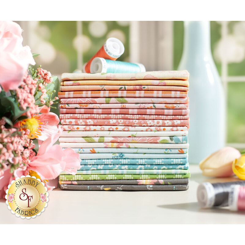 Stack of pink, yellow, peach, green, blue, and grey fabrics on a table with flowers