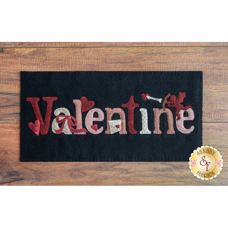Black rectangular wool mat on a brown wooden countertop with the word 