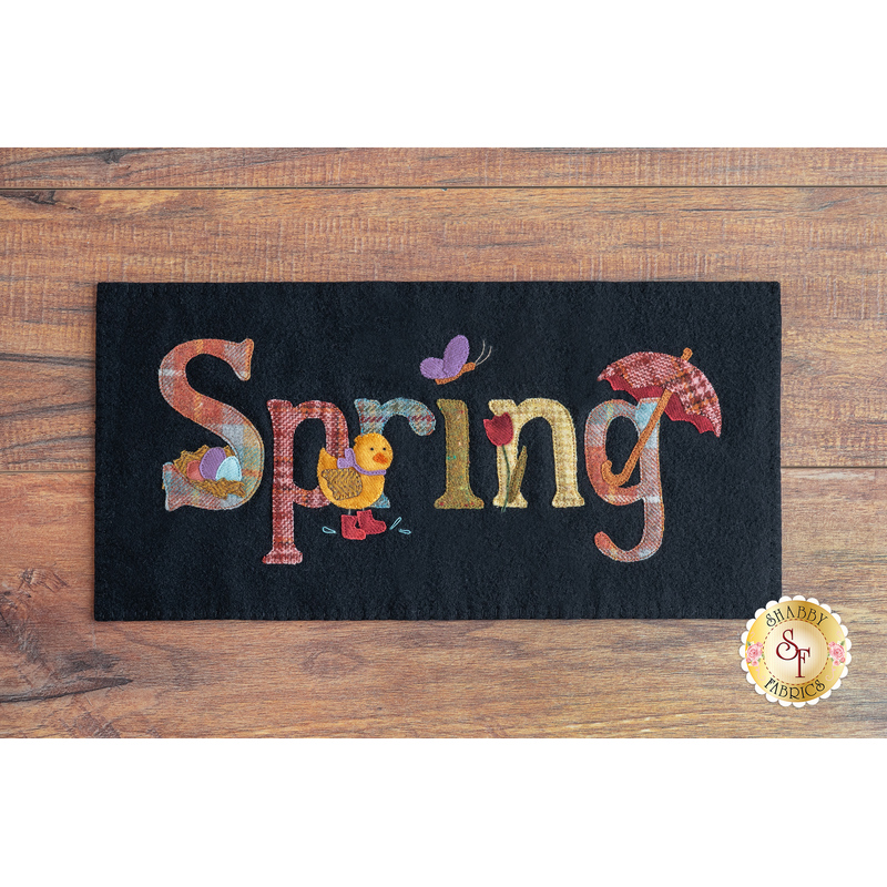 Black rectangular wool mat on a brown wooden countertop with the word 