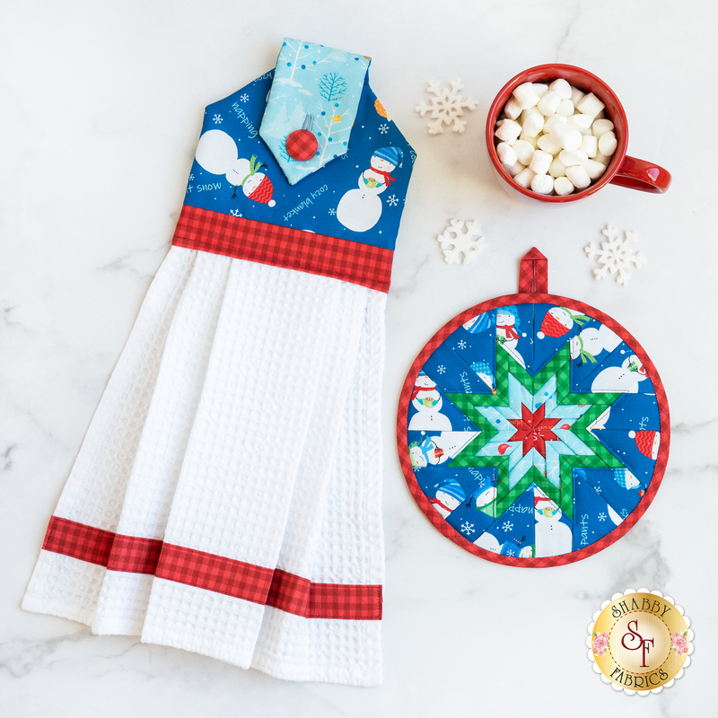 Hanging towel and hot pad for January, featuring snowmen and other winter motifs with a mug of marshmallows and snowflake decorations scattered around.