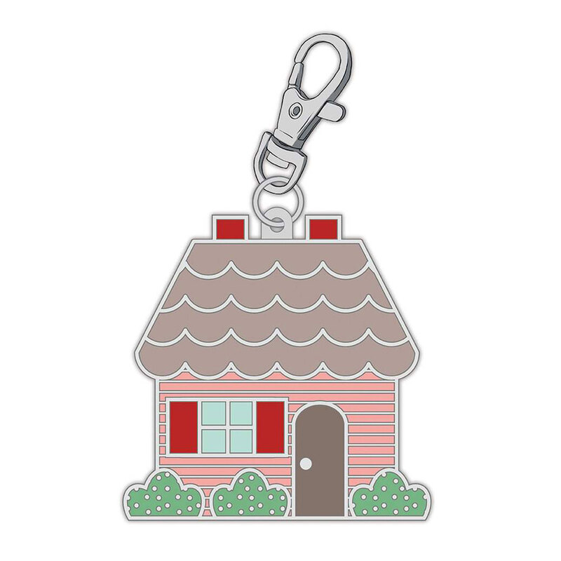 Enamel pin with a metal clip with the design of a small pink and brown house with shrubs in front of it