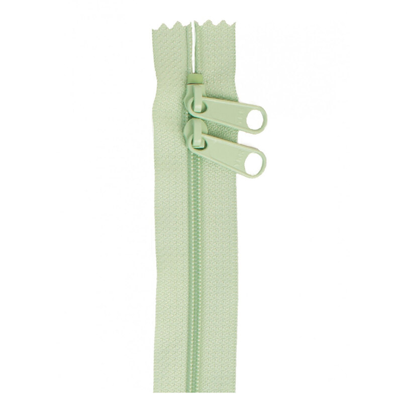 Photo of a light green zipper with two pull tabs isolated on a white background