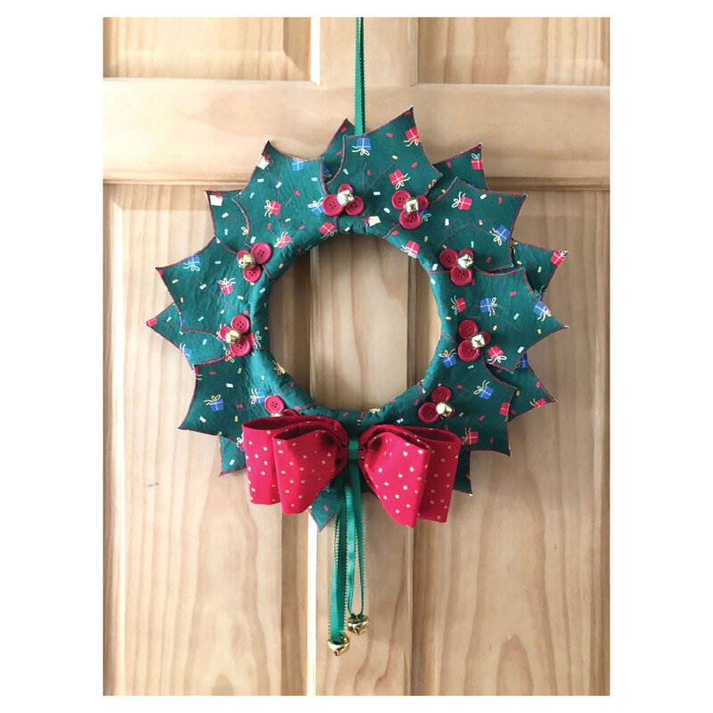 Photograph of the finished Christmas Wreath Door Hanger project, a sewn green wreath with a red bow against a maple door
