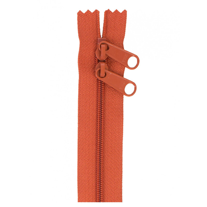 Photo of a dark orange zipper with two pull tabs isolated on a white background