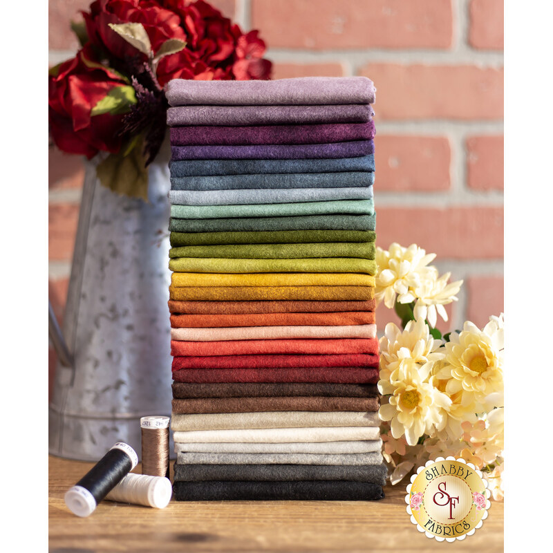 stack of colorful flannel fabrics included in the Color Wash Woolies Flannel - Refreshed FQ Set on a wood table in front of a brick wall