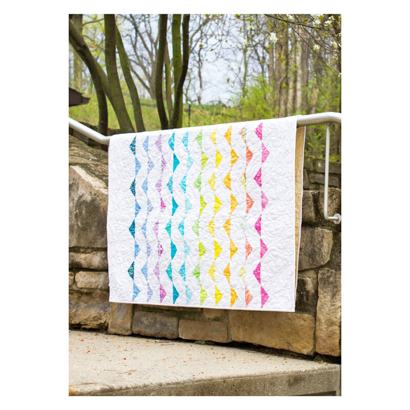 Photograph of the finished Waves quilt, a white quilt with alternating triangles in lines. The quilt is hung from a handrail on a stone stairway with trees in the background