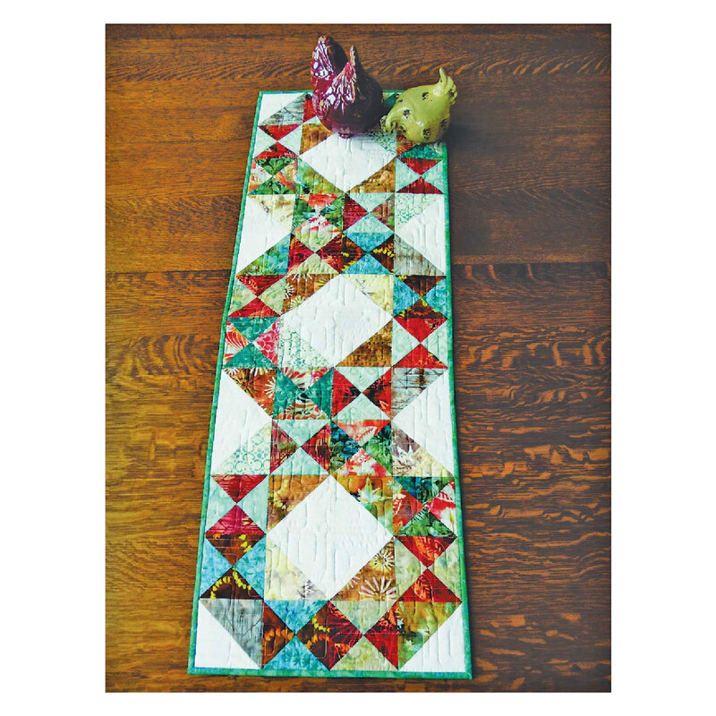 Photograph of the finished ring toss table runner, including a white background with red, teal, green, and blue triangles on it, set on a wooden table 