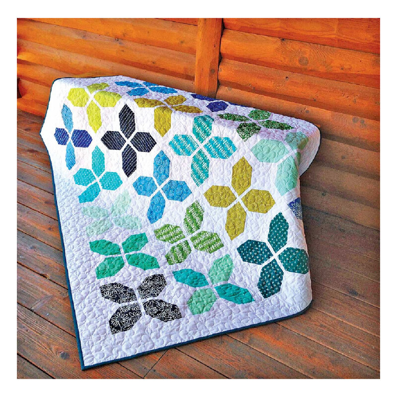 Photograph of the finished county fair quilt with a white background and cool toned piecing, set against a wood floor and log cabin background