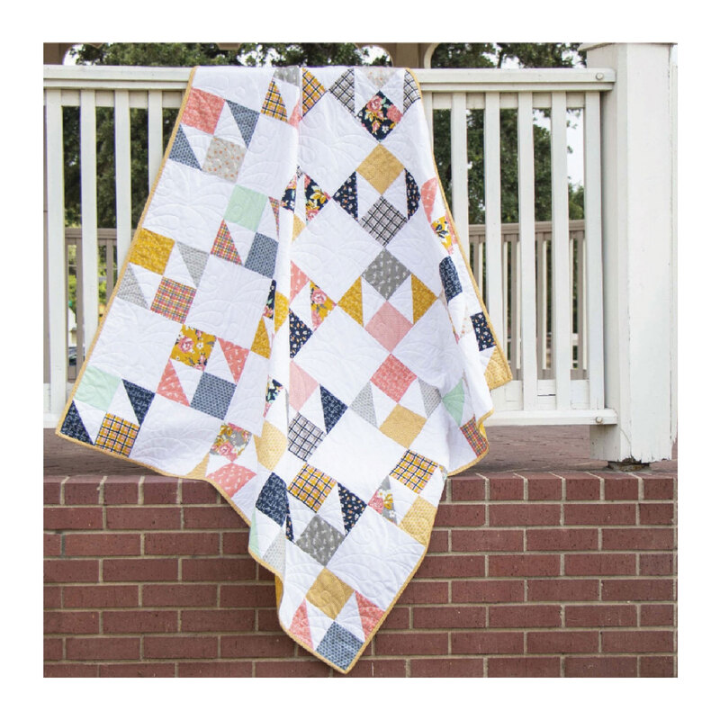 Photograph of the finished butterfly patch quilt, a white quilt with vintage colored squares and triangles, hung from a white bannister over a brick wall