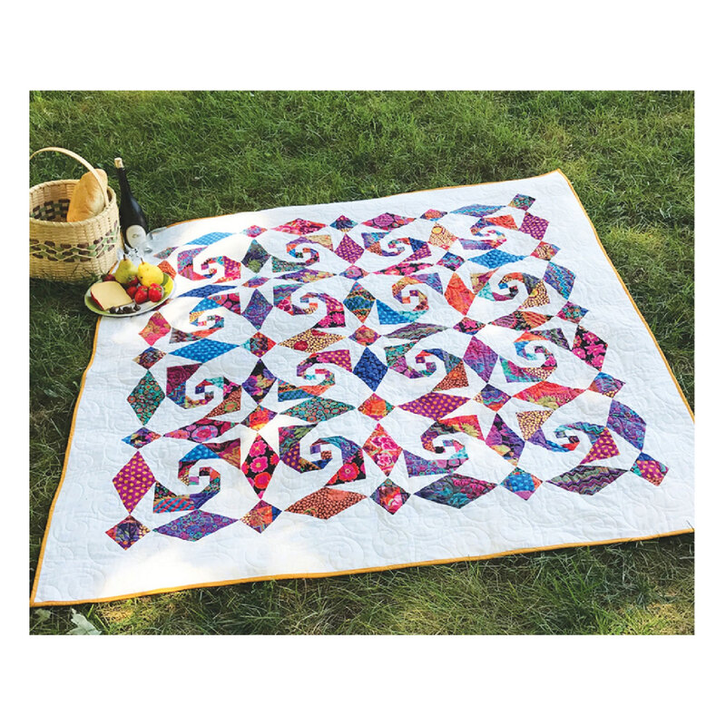 Image of a white quilt with multicolored snail blocks set on a background of grass