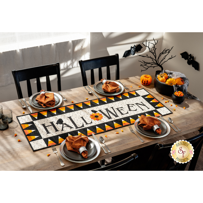 A photo of a dining table with hallloween themed place settings and a table runner with a candy corn border and the word 