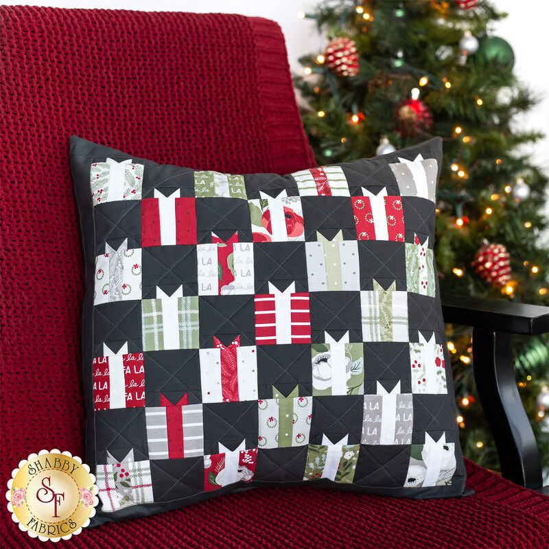 Photo of a chair with a red blanket draped over it with a decorated christmas tree in the background and a pillow featuring small quilted gifts motifs all over.
