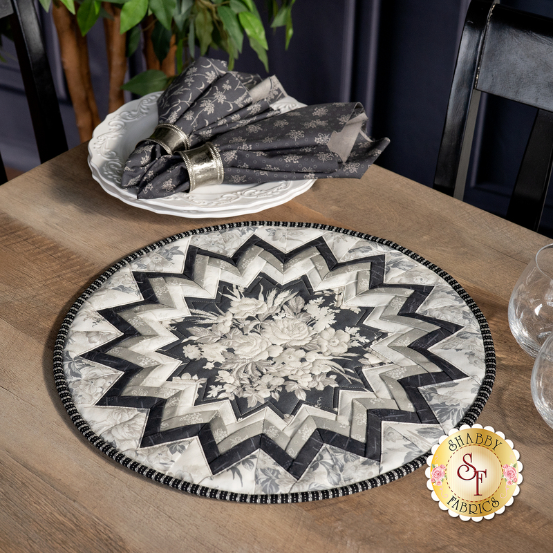 Photo of a black, white, and grey table topper on a brown wooden table with a stack of white plates and matching napkins in the background