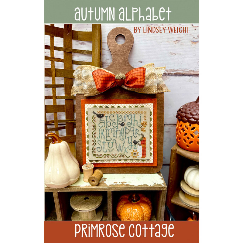 Front of the Autumn Alphabet pattern, showcasing the completed fall-themed alphabet sampler, placed on a vintage shelf, with ceramic pumpkins and wooden spools of thread