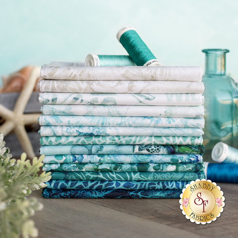 A photo of a stack of sea inspired fabrics in the Sea Breeze collection, in shades of blue, white, teal, and aqua