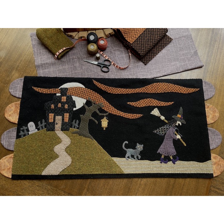 Close up of Halloween wool mat with a witch, broom, and cat behind her