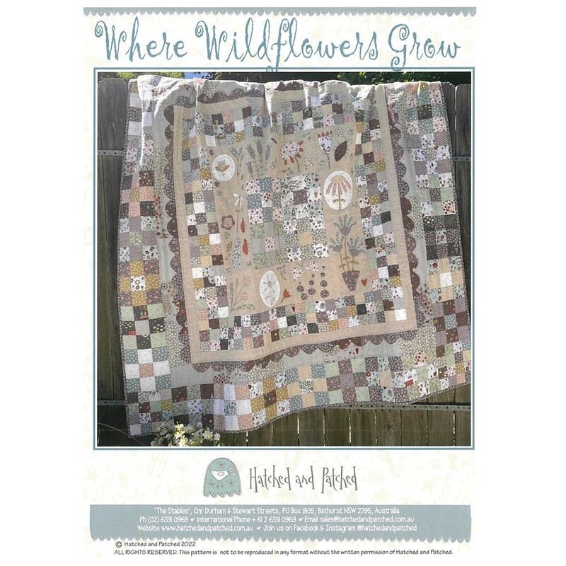 Front of Where Wildflowers Grow pattern, showcasing a beautiful embroidered and patchwork quilt with a variety of button flowers, staged over a wool panel fence