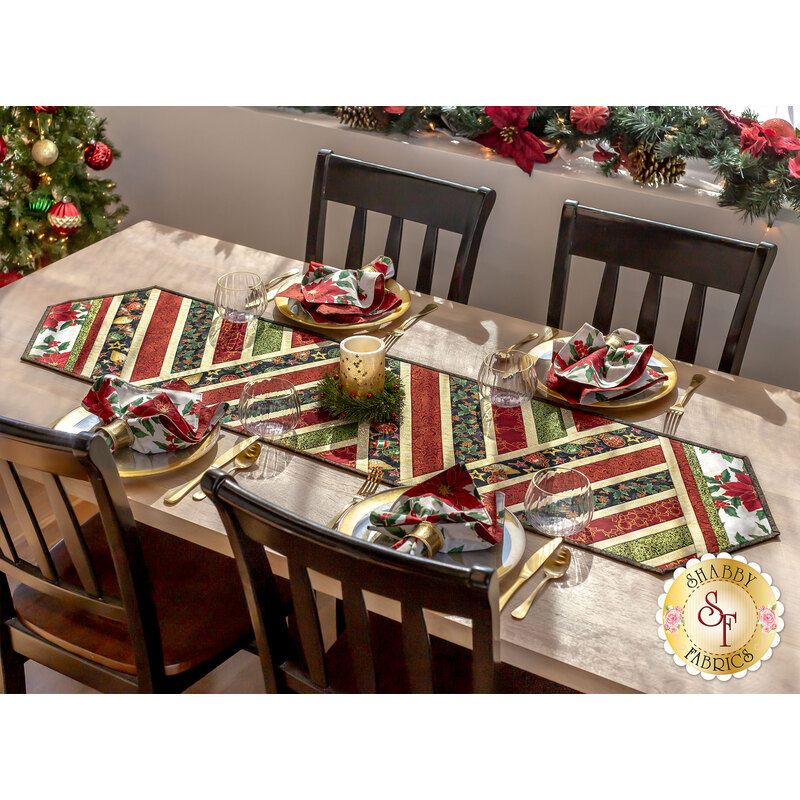 Photo of finished table runner on a long wooden table with four place settings and chairs in a room with garland in the background and a decorated Christmas tree at one side