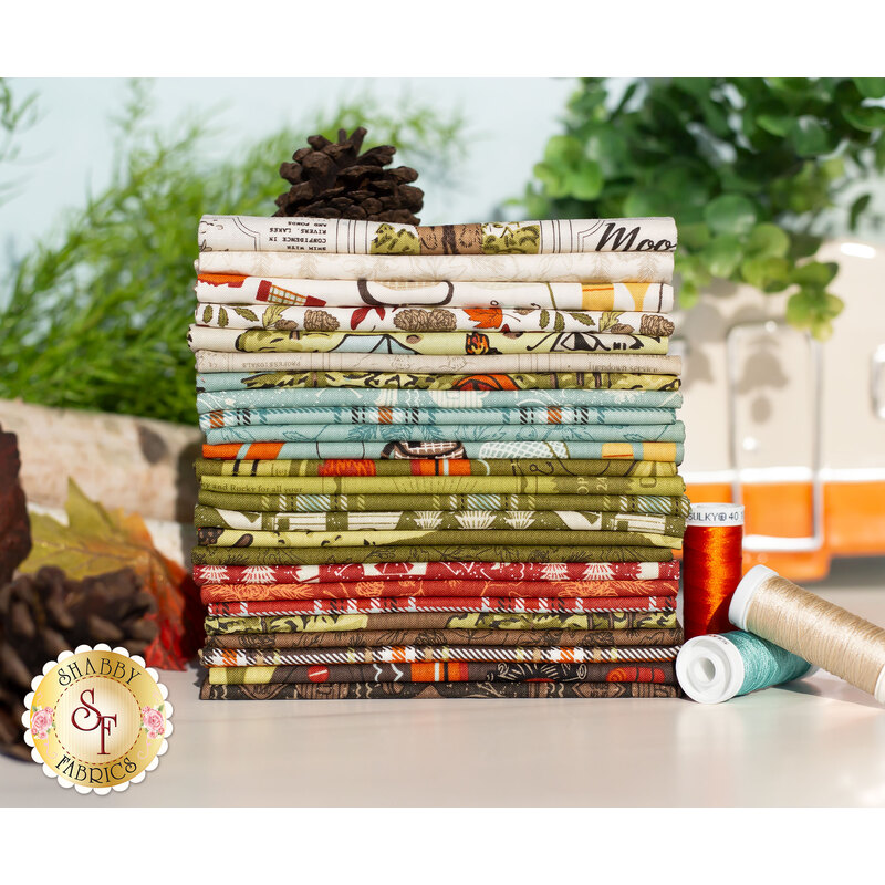 the great outdoors fat quarter set, with camping and nature motifs, in shades of aqua, cream, green, red, and brown, stacked on a table surrounded by greenery, thread, leaves and small decorative camp trailer