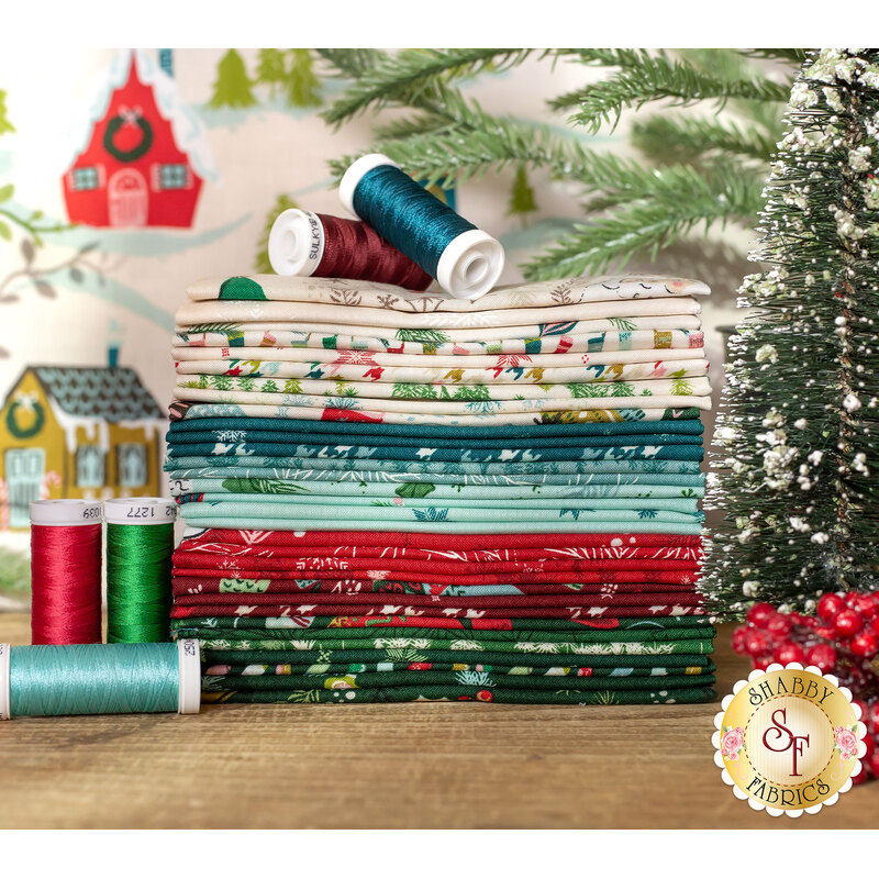cozy wonderland fabric, in shades of red, dark red, dark blue, blue green, and creme, of Christmas themed designs and patterns on a wood table surrounded by thread and evergreens