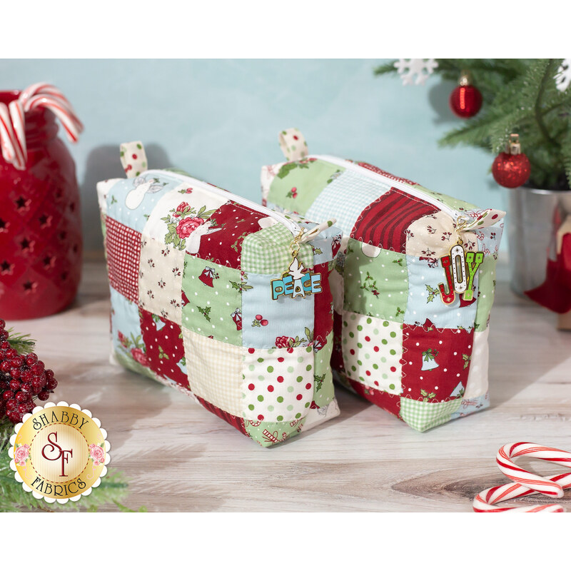 Photo of mini-charm bags made with the I Believe in Angels collection atop a wooden countertop in front of a blue wall with Christmas decor like a small decorated tree, candy canes, foliage, and a red jar