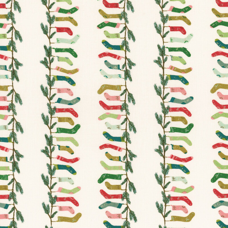 natural white fabric with rows of fir branches with hanging stockings in shades of pink, red, green, and aqua