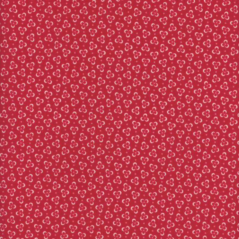 Red fabric with light pink three-petaled flowers arranged in a ditsy print 