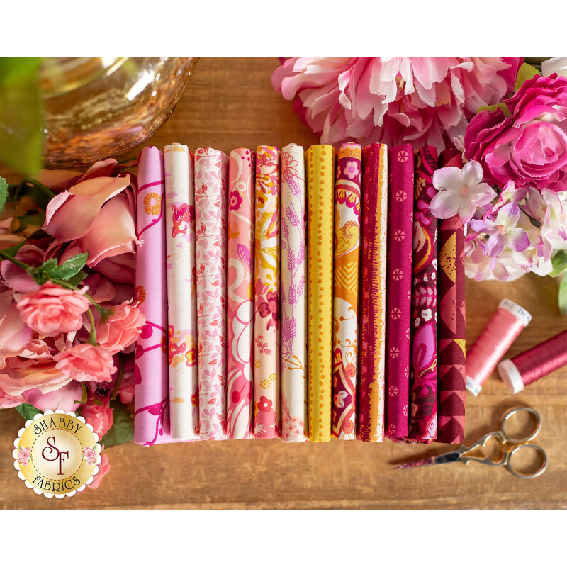 pink, fuchsia, and gold floral fabrics on a wood table surrounded by flowers and thread