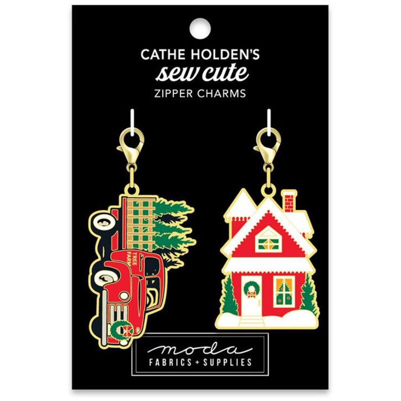 Two charms hung from the black tag packaging, a red truck with trees in the bed and a snowy red house