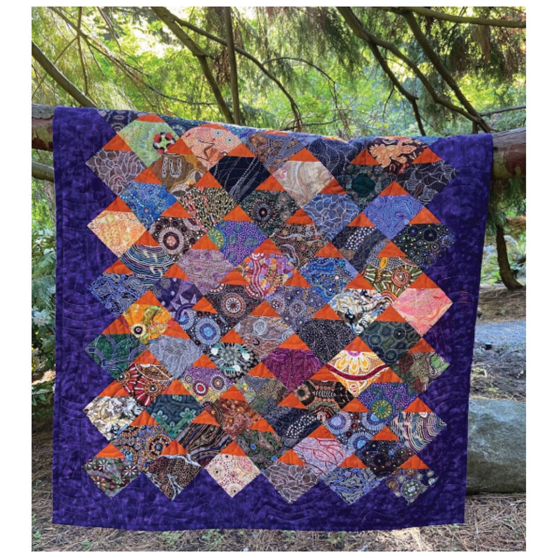 Front of pattern showing finished quilt, draped over a tree branch in a dense wood