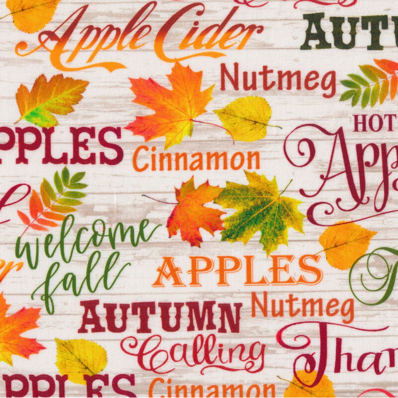 White wood-textured fabric featuring leaves, and autumn related sayings in red, green orange, and yellow