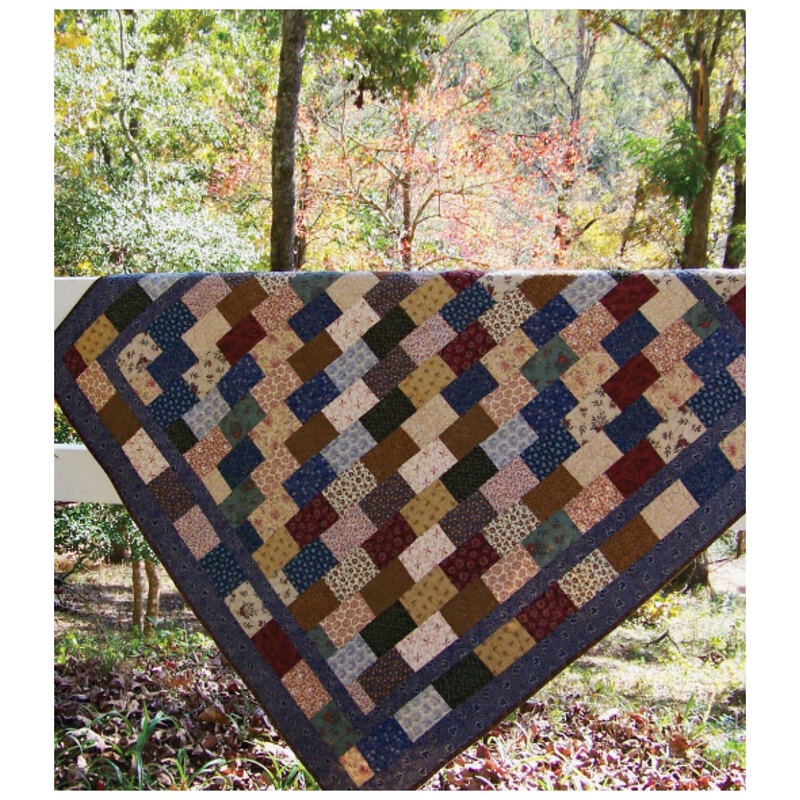 The finished postcard quilt in muted tones, draped over a railing outside, with trees in the background