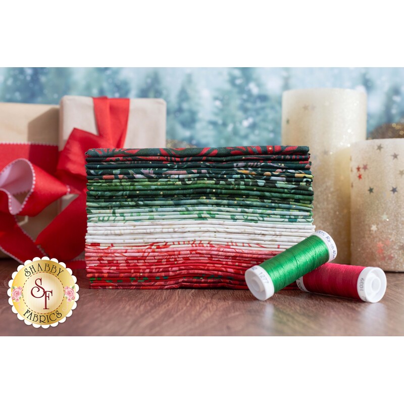 A stack of green, red, and cream fabrics displayed on a table with coordinating thread and candles.