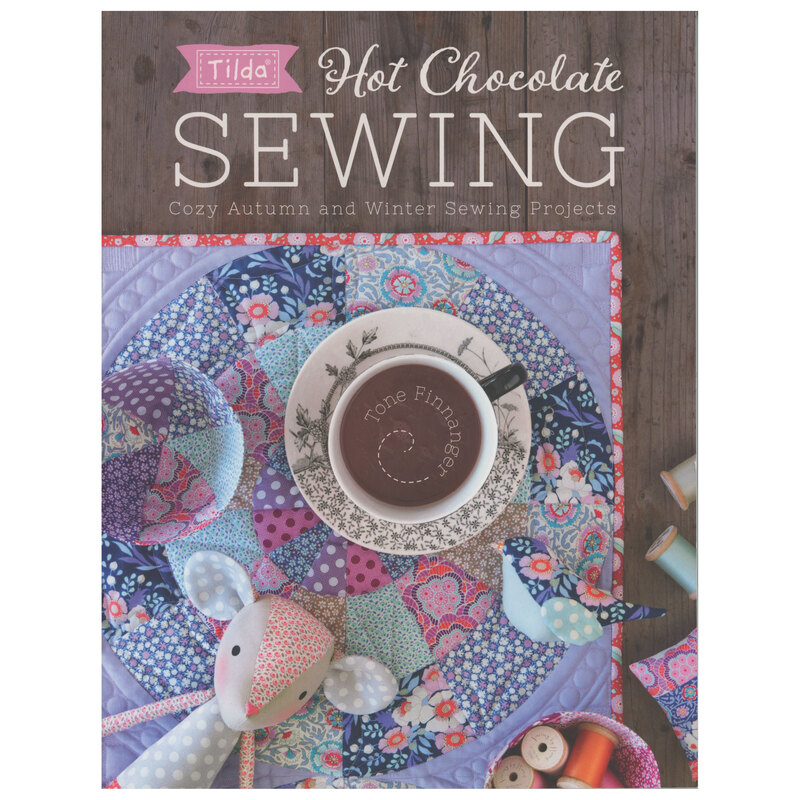 Front cover of the pattern book showing a beautiful table topper with a cup of hot chocolate on top, surrounded by other small projects from the book