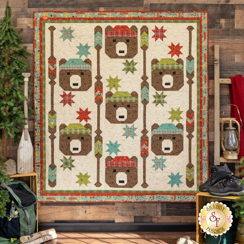 The completed Paddling Bears Quilt in The Great Outdoors, staged against rustic wood paneling beside cabin furniture and camping paraphernalia. 