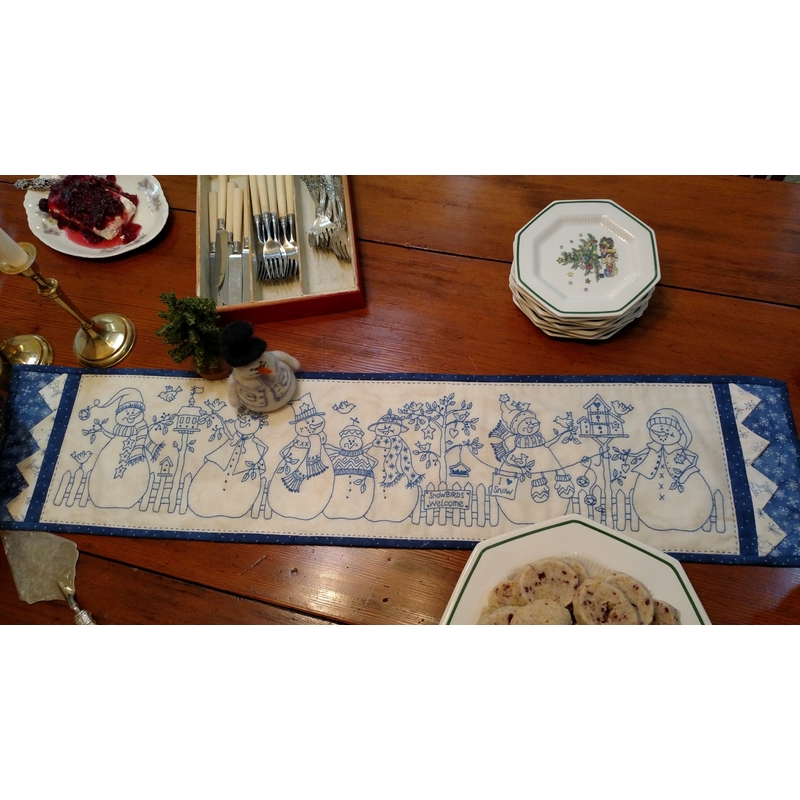 The completed Yard of Snowmen table runner, staged on a table among silverware, plates, and treats.