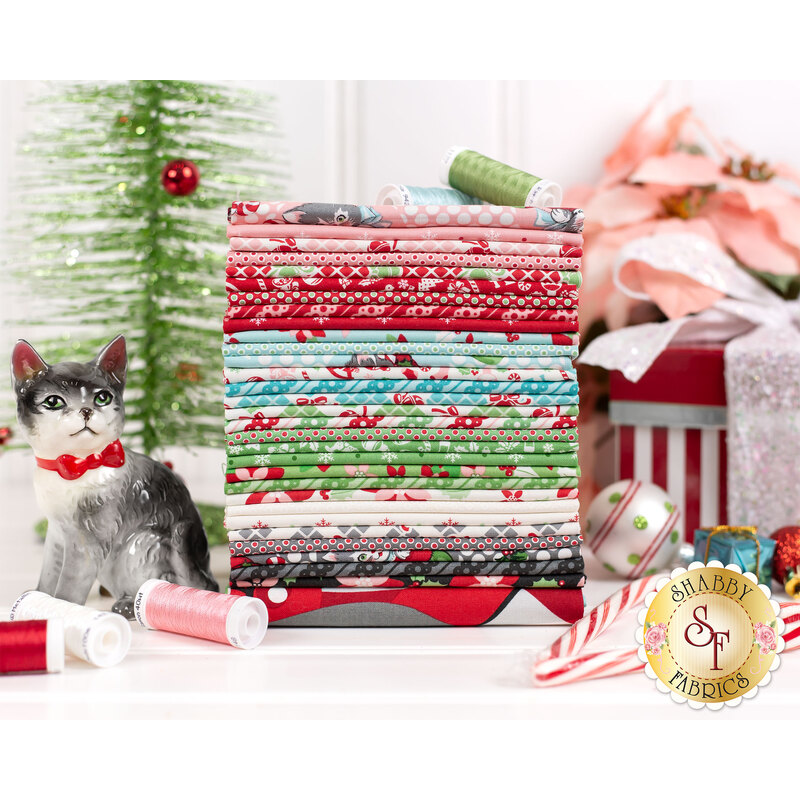 Kitty Christmas fabric collection stacked next to a cat figurine, in front of a Christmas tree, pink poinsettias, and a gift box