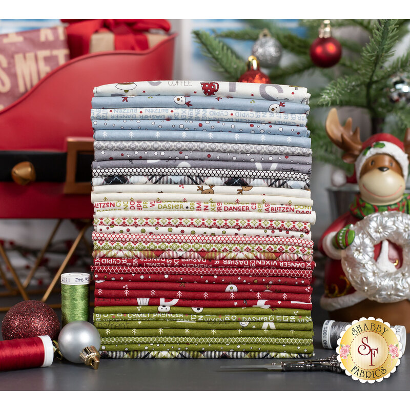 On Dasher fabrics in muted shades of icy blue, white, red, and green on a grey table with a reindeer and sleigh and christmas tree