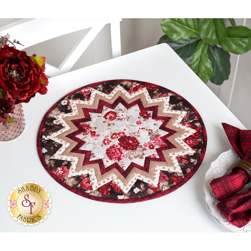 Photo of a floral table topper on a white table with red roses and white plates with red cloth napkins and a houseplant in the background