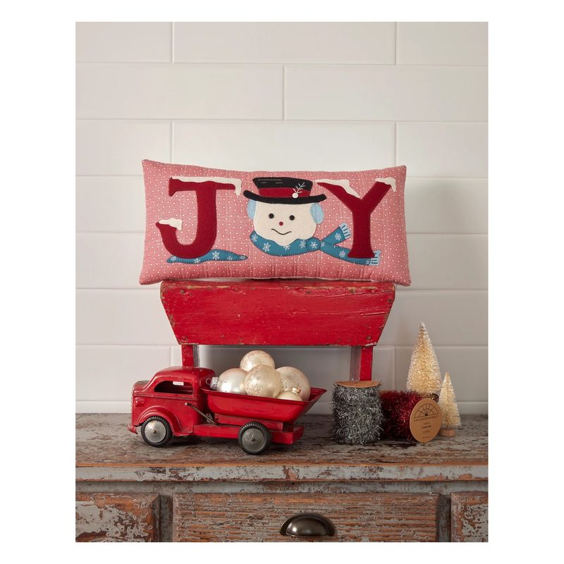 Cover photo of the pattern, showing the completed pillow project staged on a rustic red wood table beside a red truck holding ball ornaments.